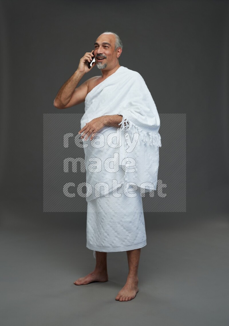 A man wearing Ehram Standing talking on phone on gray background