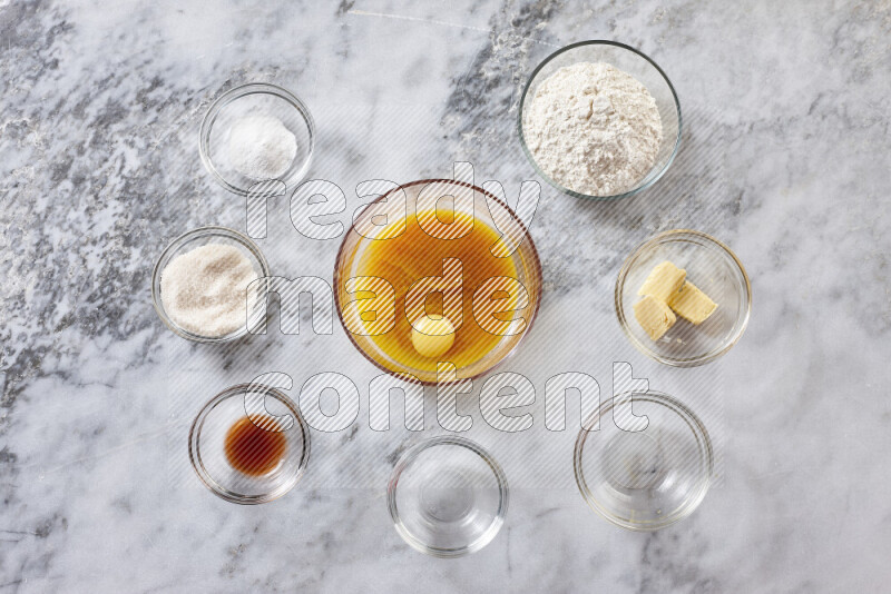 كوكيز خطوة بخطوة بمكوناتها، الدقيق، الزبدة، السكر البني، البيض، الفانيليا، السكر الأبيض، رقائق الشوكولاتة وصودا الخبز على خلفية رخام رمادي