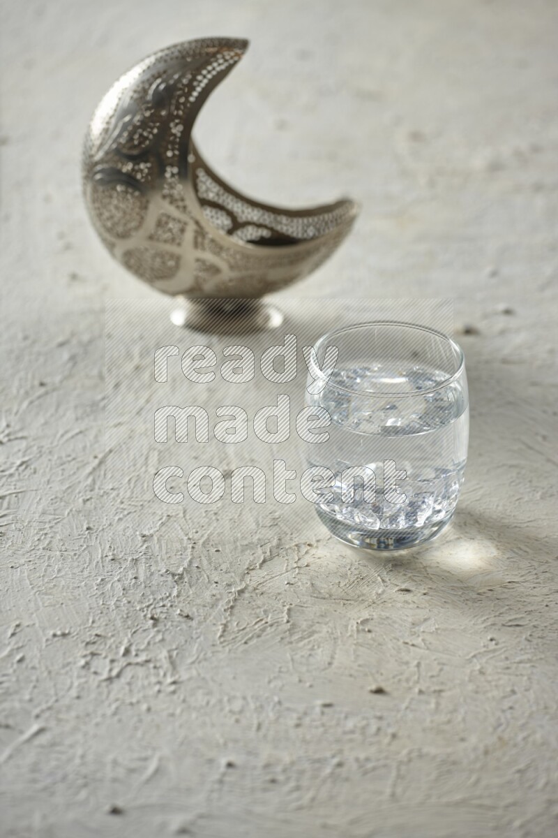 A silver lantern with different drinks, dates, nuts, prayer beads and quran on textured white background