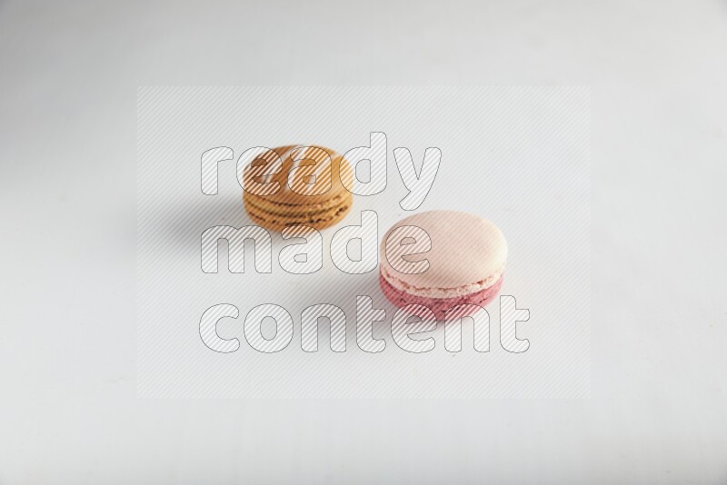 45º Shot of of two assorted Brown Irish Cream, and Pink Litchi Raspberry macarons on white background