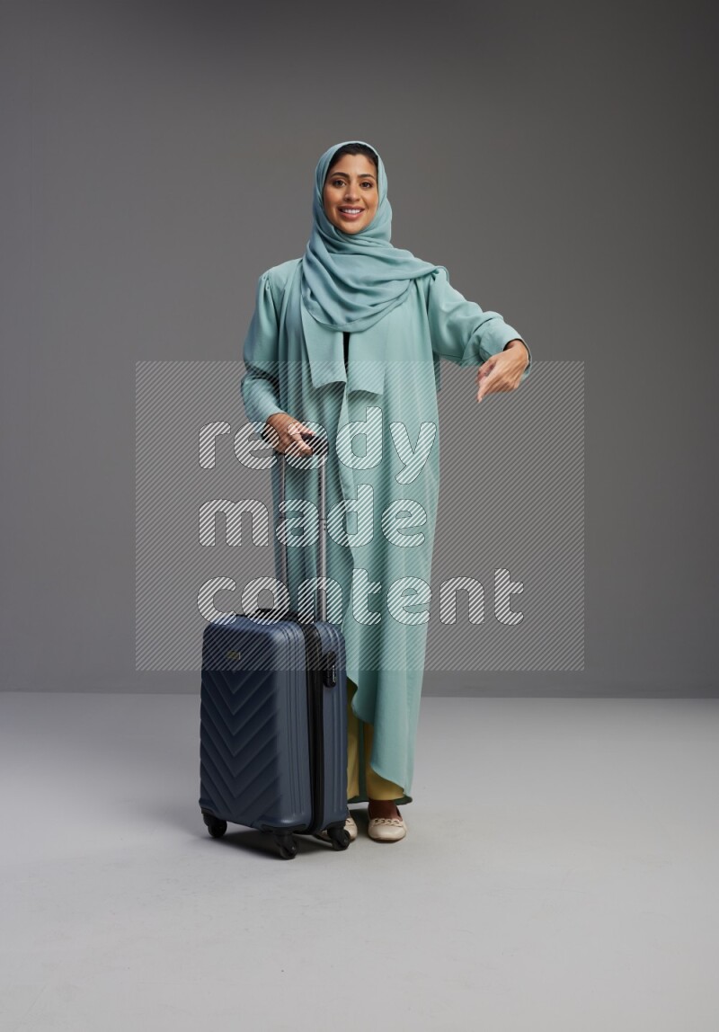 Saudi Woman wearing Abaya standing holding Travel bag on Gray background