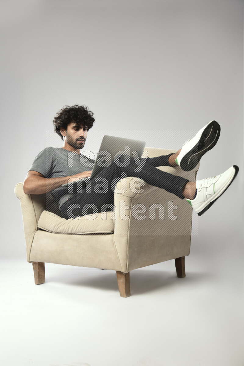 A man wearing casual sitting on a chair working on a laptop on white background