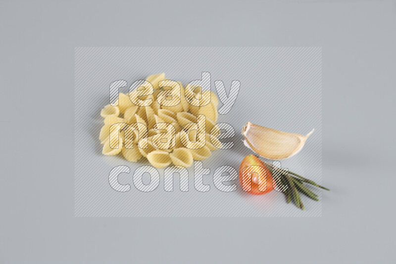 Raw pasta with different ingredients such as cherry tomatoes, garlic, onions, red chilis, black pepper, white pepper, bay laurel leaves, rosemary, cardamom and mushrooms on light blue background