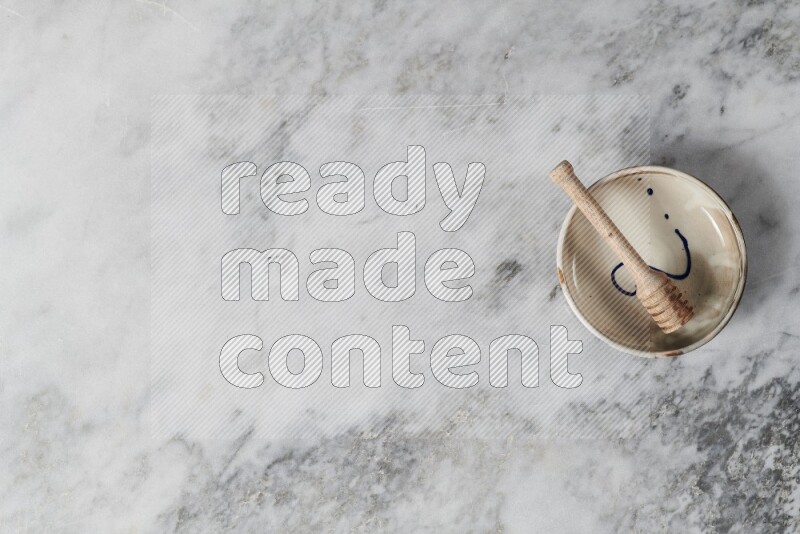 Multicolored pottery bowl with wooden honey dipper in it on grey marble background