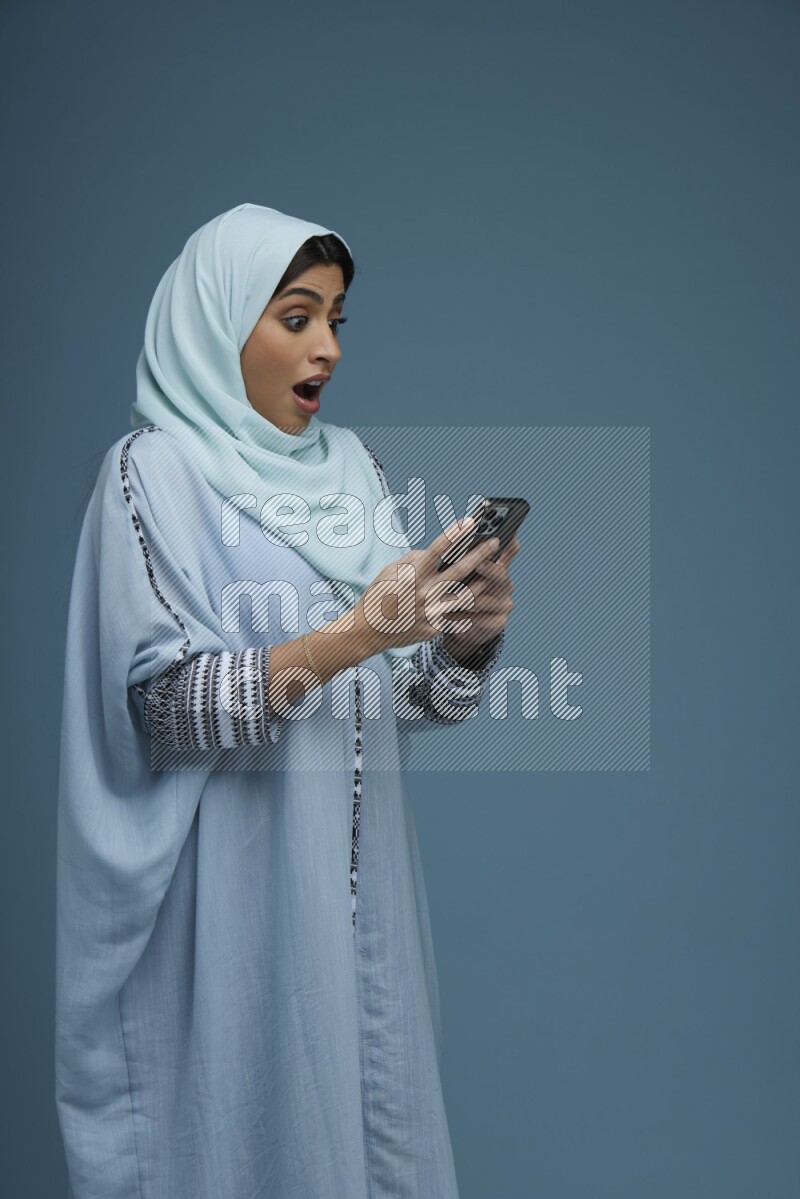 A Saudi woman Texting in a blue background wearing a blue Abaya with hijab