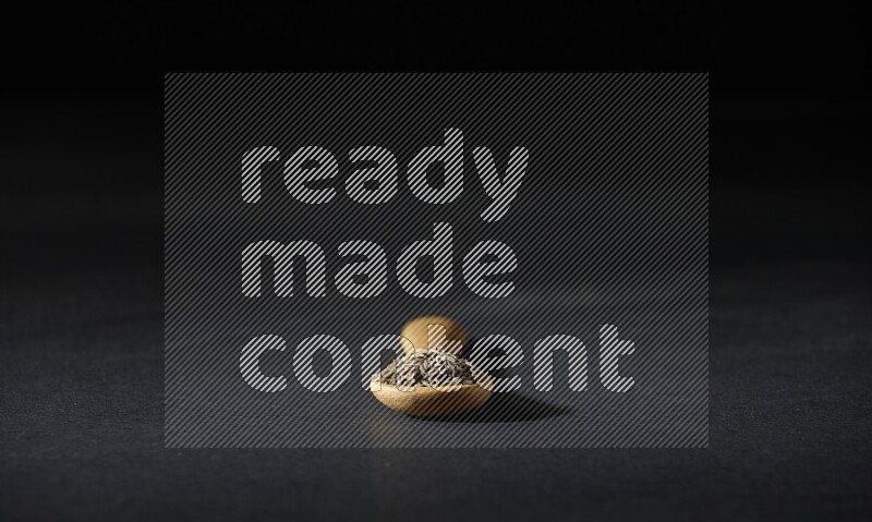 A wooden spoon full of cumin seeds on black flooring