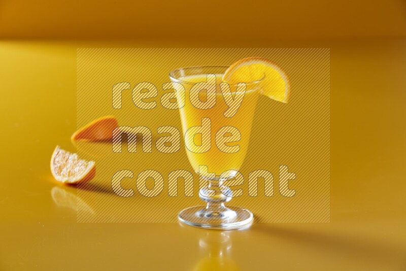 glass of orange juice with orange slice on yellow background