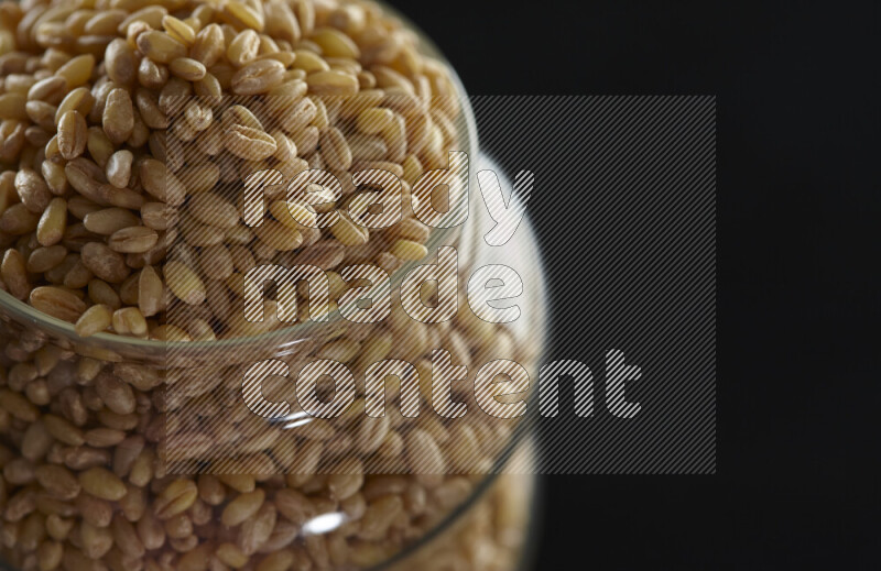 Hulled wheat in a glass jar on black background