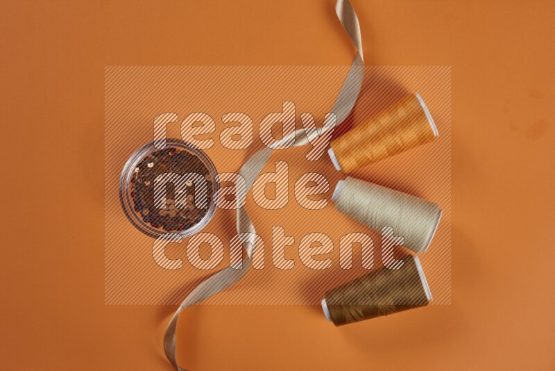 A brown collection of sewing and tailoring tools arranged on a orange background