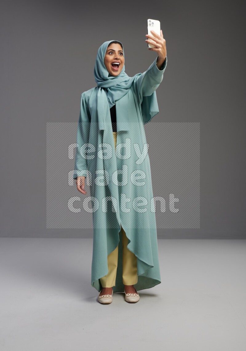 Saudi Woman wearing Abaya standing taking selfie on Gray background