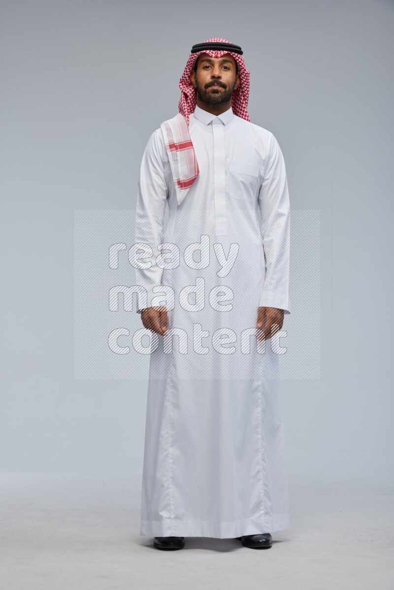 Saudi man Wearing Thob and shomag standing interacting with the camera on Gray background