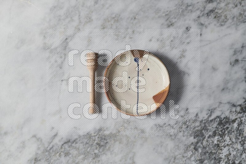 Multicolored pottery plate with wooden honey dipper on the side on grey marble background