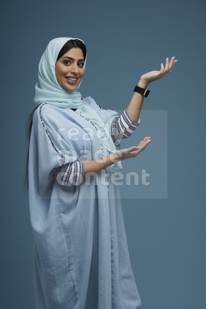 A Saudi woman pointing in a blue background wearing a Blue abaya