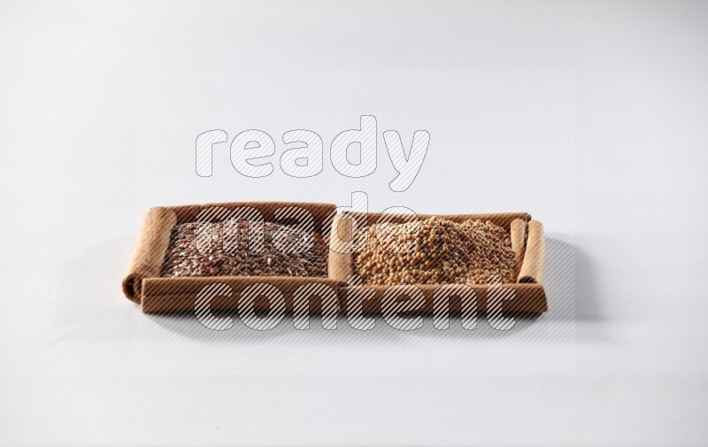 مربعان من أعواد القرفة ممتلئان بحبوب الخردل وبذور الكتان علي خلفية بيضاء