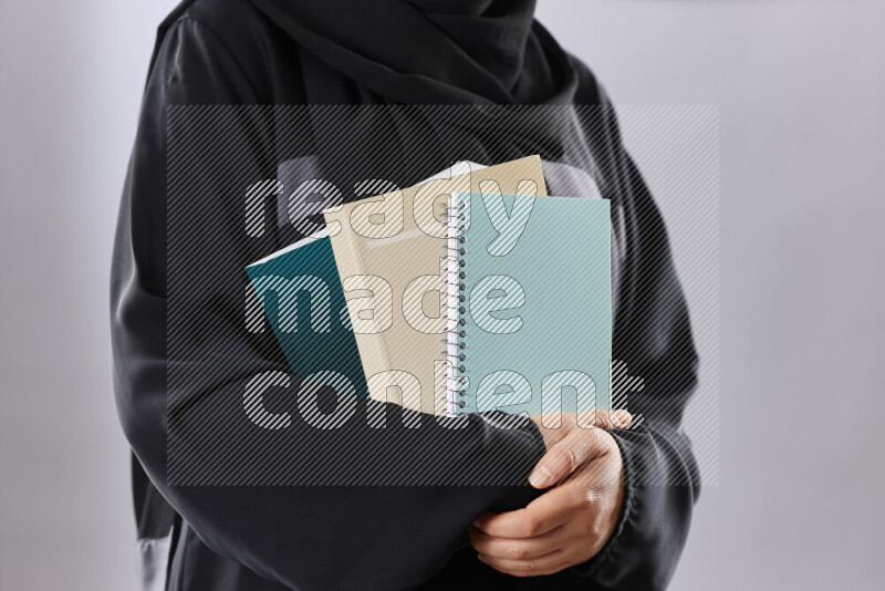 A woman in abaya holding books and a board in different positions (back to school)
