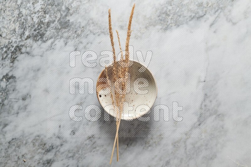 Wheat stalks on multicolored pottery plate on grey marble background