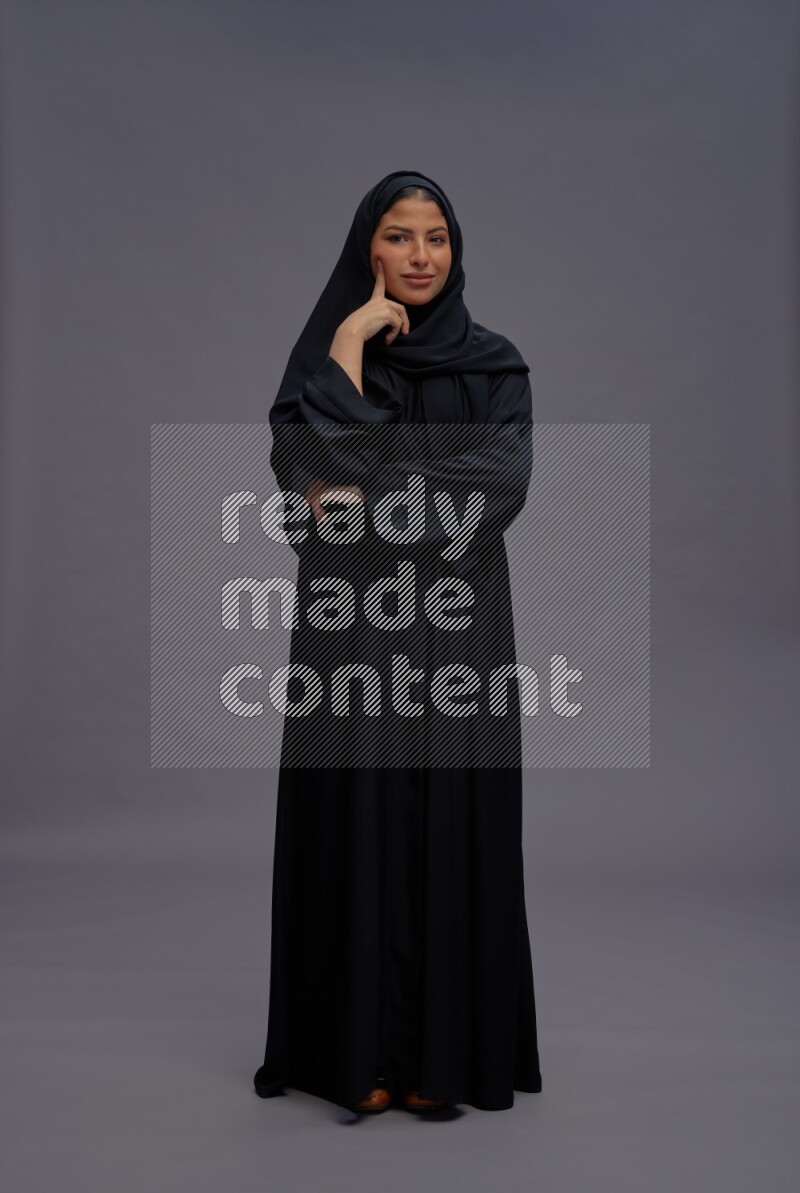 Saudi woman wearing Abaya standing interacting with the camera on gray background