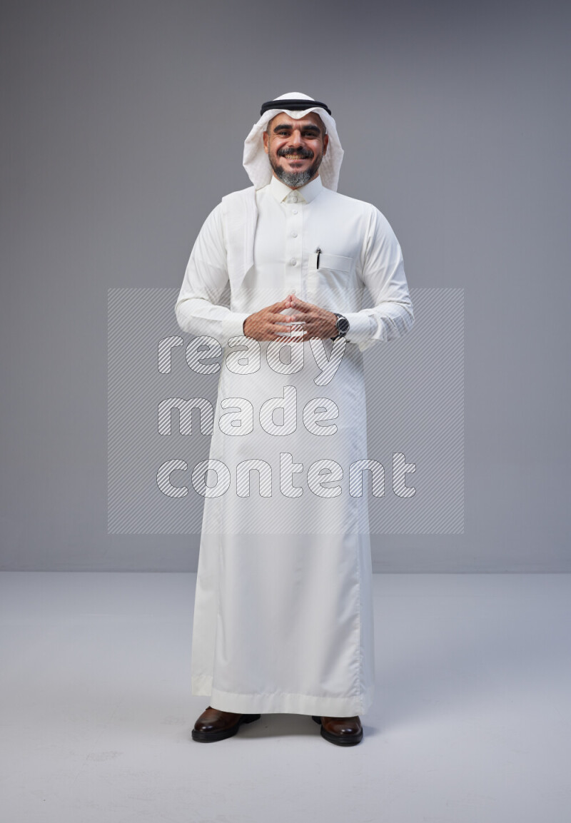 Saudi man Wearing Thob and white Shomag standing interacting with the camera on Gray background