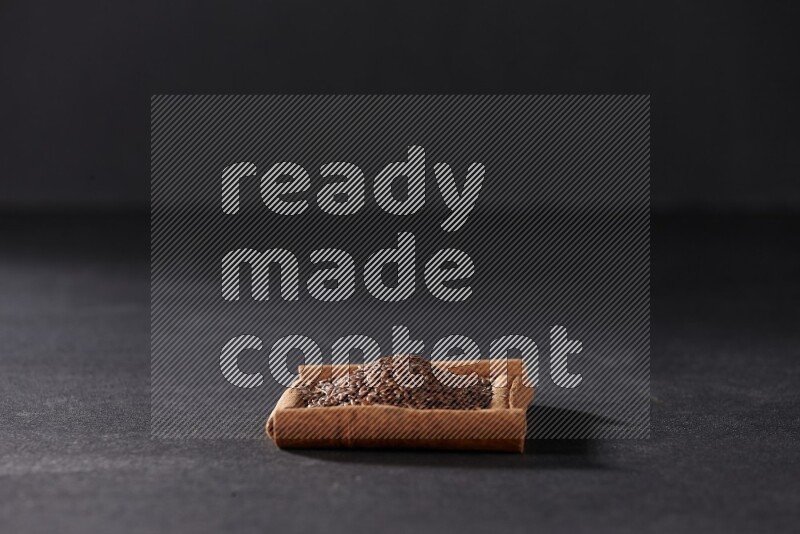 A single square of cinnamon sticks full of flaxseeds on black flooring