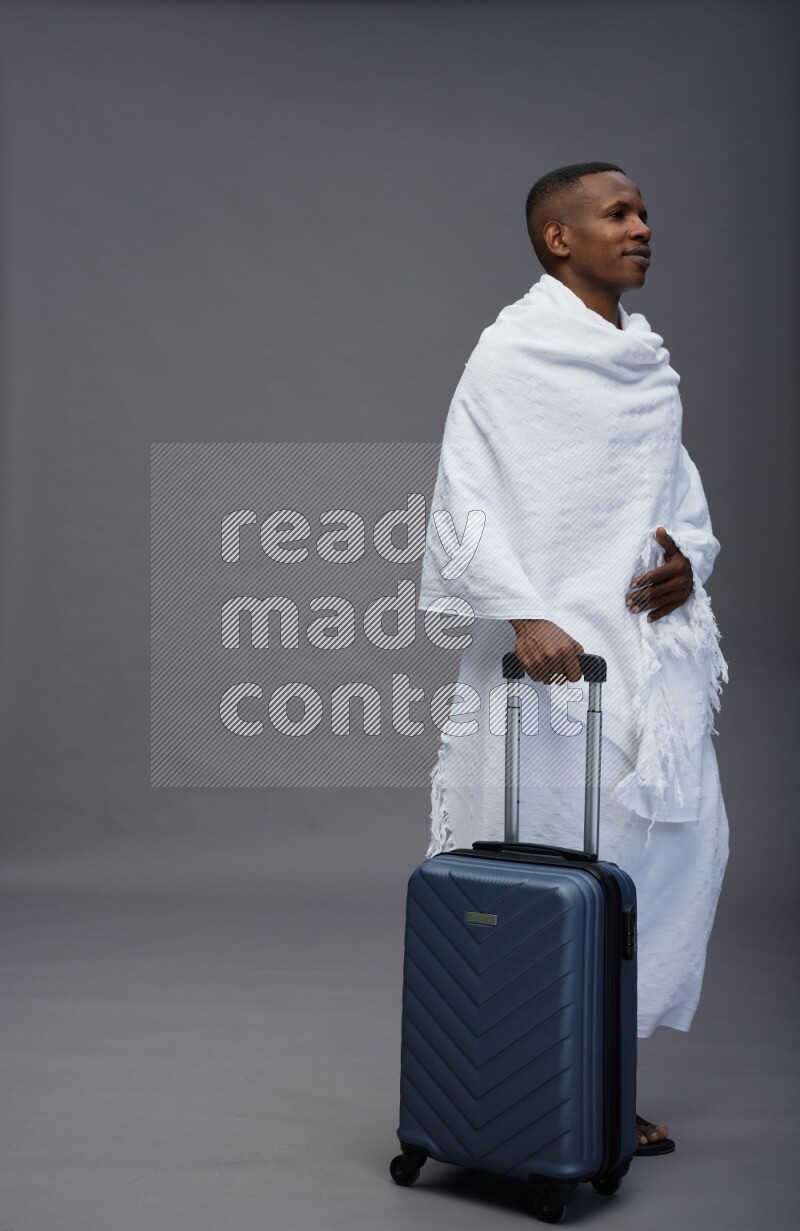 A man wearing Ehram Standing holding traveling bag on gray background