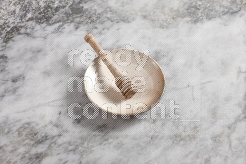 Beige pottery plate with wooden honey dipper in it on grey marble background