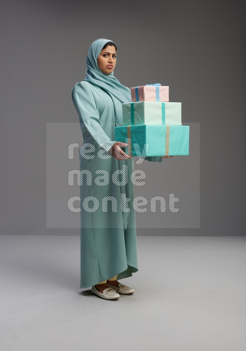 Saudi Woman wearing Abaya standing holding gift box on Gray background