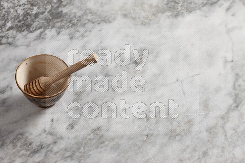 Decorative pottery bowl with wooden honey dipper in it on grey marble background