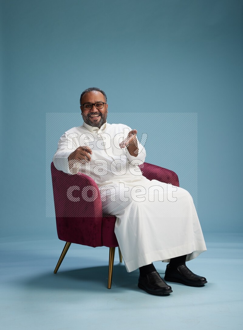 Saudi Man without shimag sitting on chair holding ATM card on blue background
