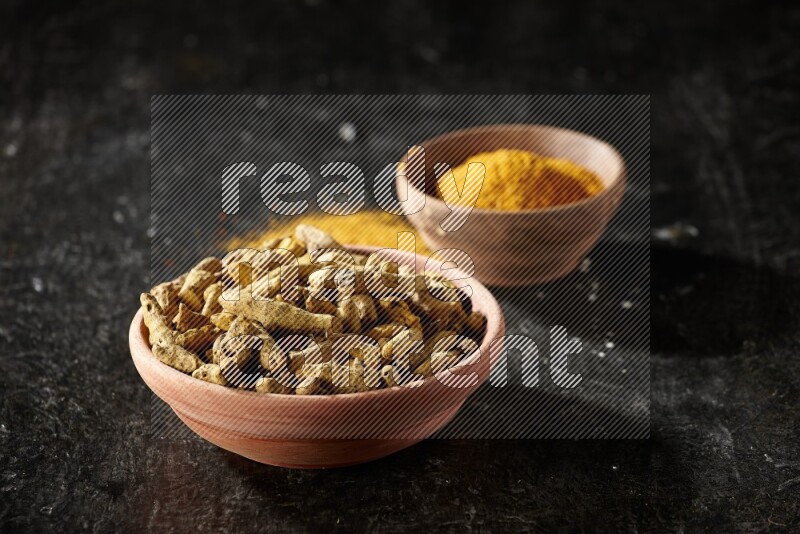 وعاءان خشبيان، أحدهما ممتلئ ببودرة الكركم والآخر بأصابع الكركم المجففة، على خلفية سوداء