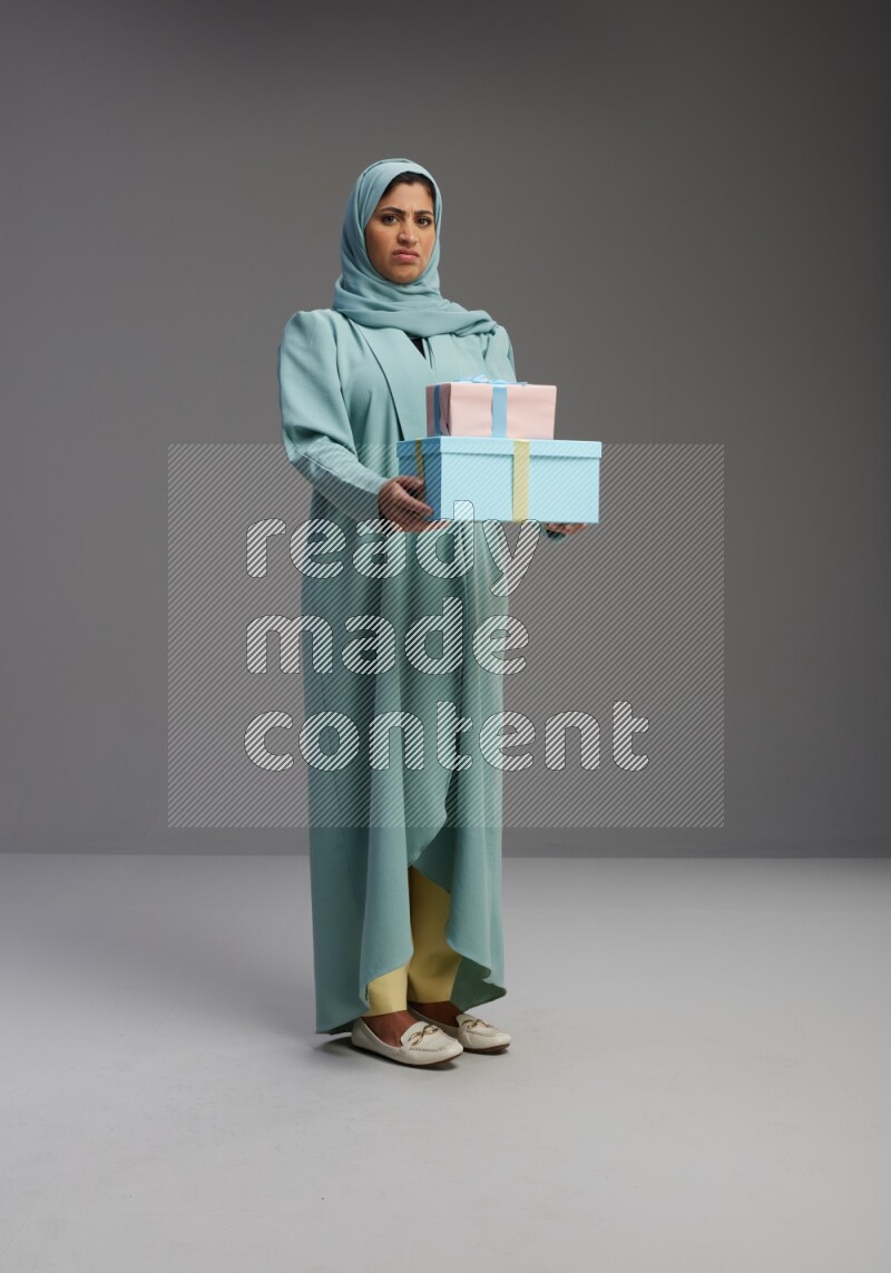 Saudi Woman wearing Abaya standing holding gift box on Gray background