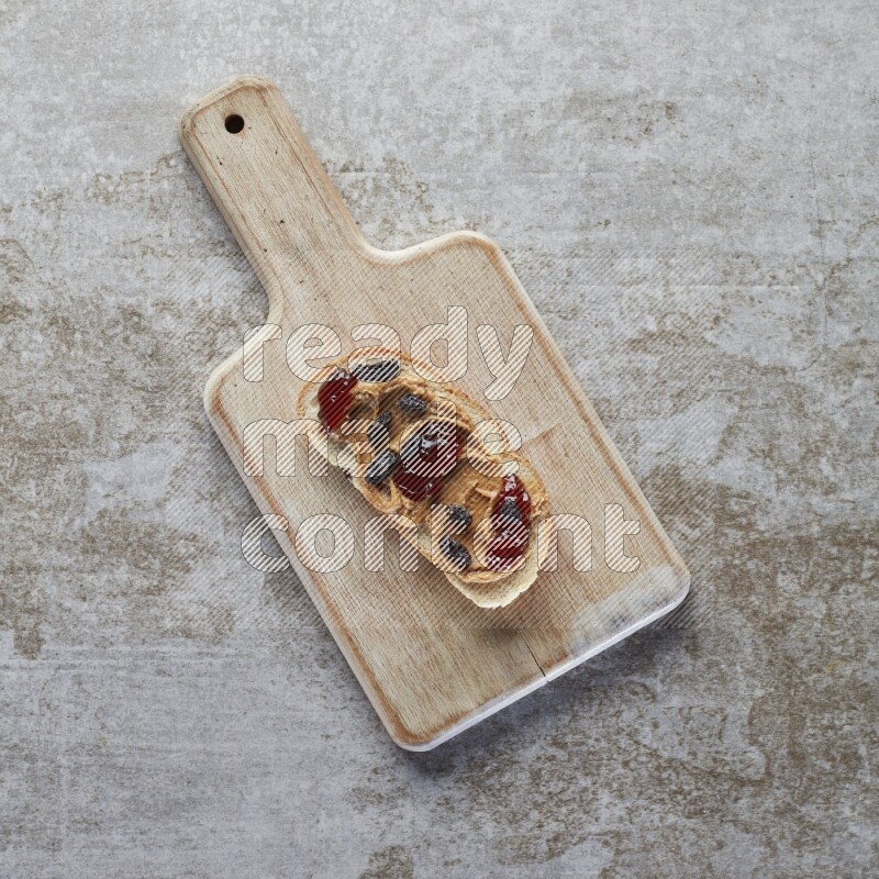 open faced peanut butter sandwich with jam and dried cranberries on a grey textured background