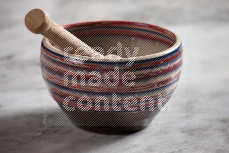 Multicolored pottery bowl with wooden honey dipper in it on grey marble background