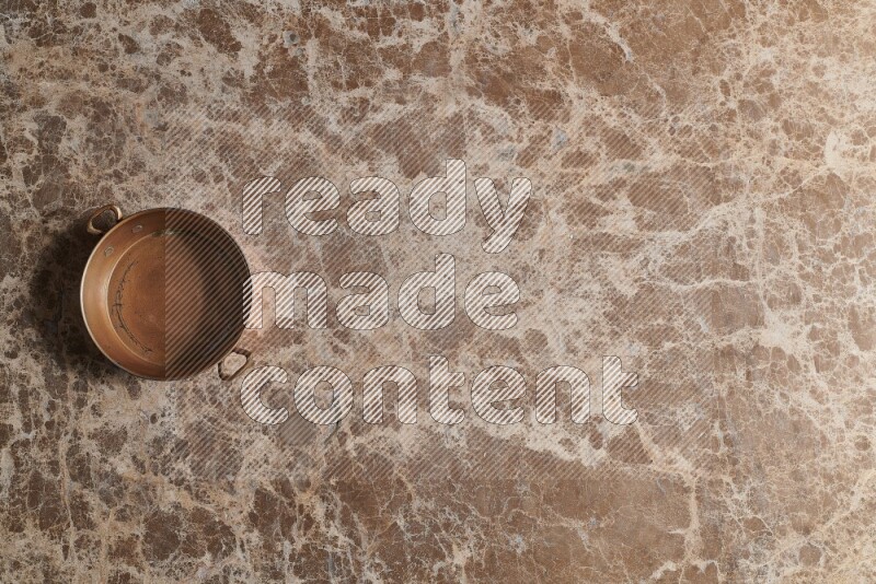 A small copper pan on beige marble background