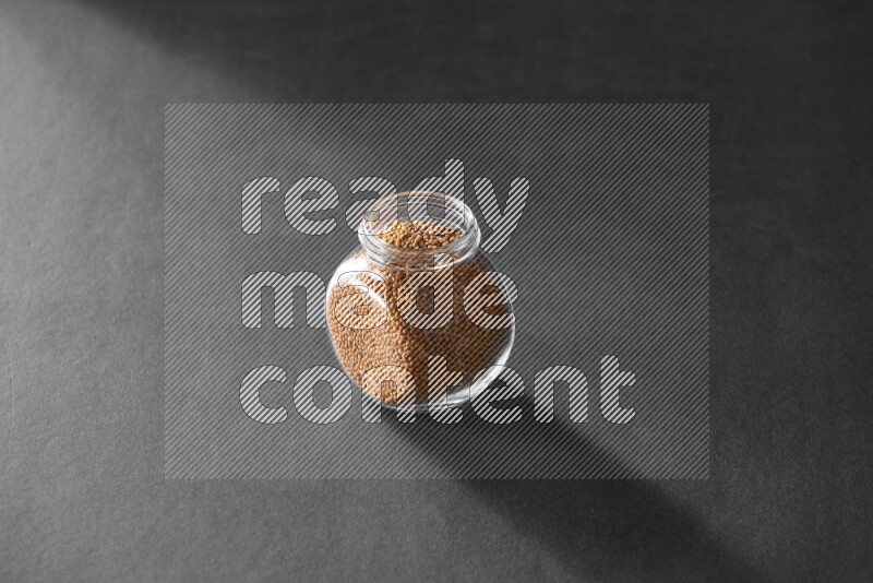 A glass spice jar full of mustard seeds on black flooring