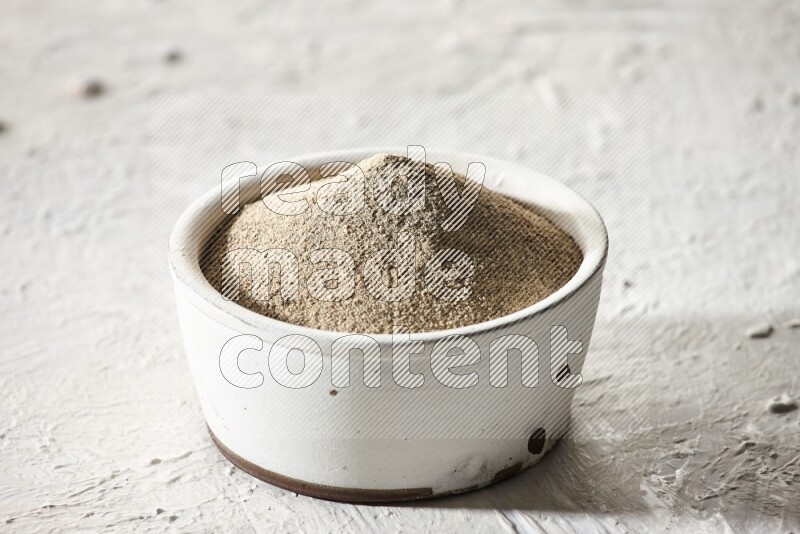 white pottery bowl full of white pepper powder on textured white flooring