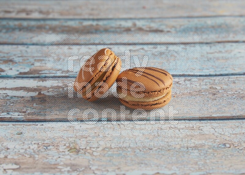 45º Shot of of two assorted Brown Irish Cream, and light brown Almond Cream macarons next to each other on light blue background