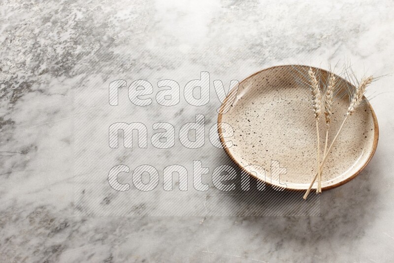 Wheat stalks on multicolored pottery plate on grey marble background