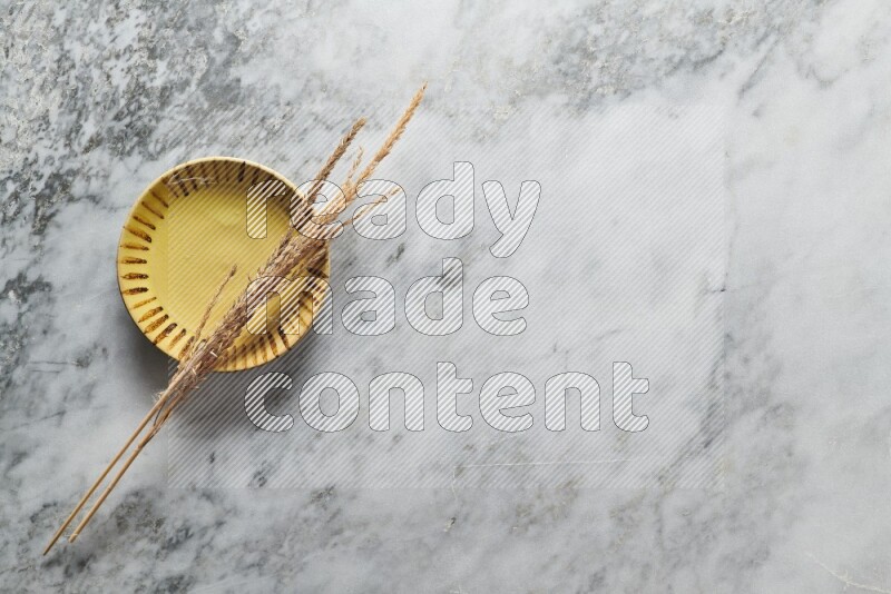 Wheat stalks on multicolored pottery plate on grey marble background