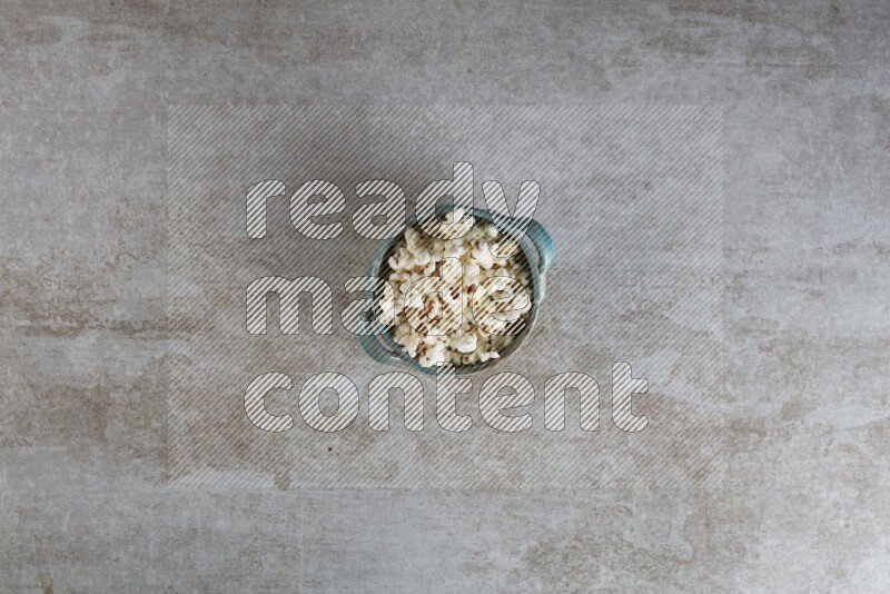 popcorn in a multi-colored handheld ceramic bowl on a grey textured countertop