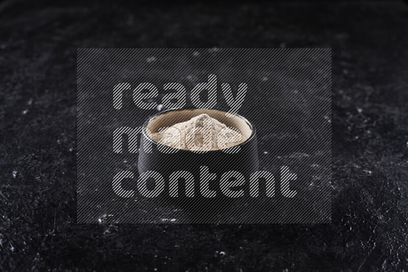 A black pottery bowl full of onion powder on black background