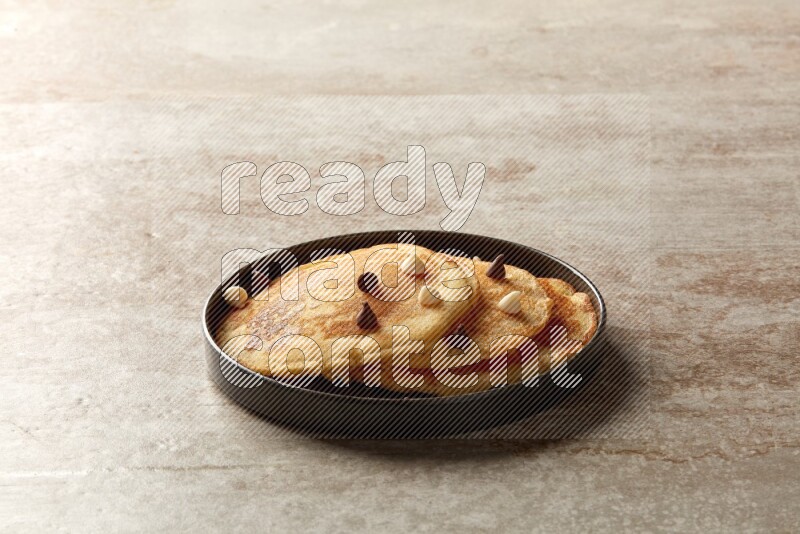 Three stacked chocolate chips pancakes in a black plate on beige background