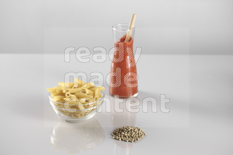 Raw pasta with tomatoe pasta with different ingredients such as cherry tomatoes, basil, garlic, bay laurel, cardamom, white pepper, black pepper, red chilis and wheat stalks on light grey background