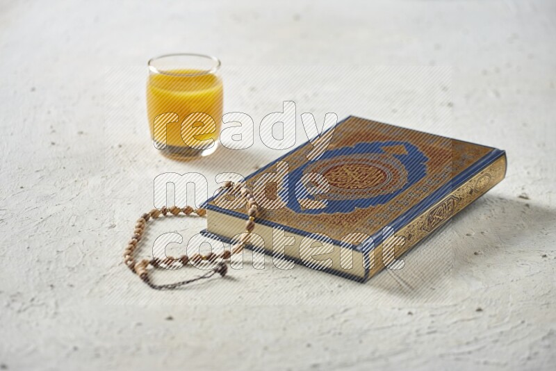 Quran with dates, prayer beads and different drinks all placed on textured white background