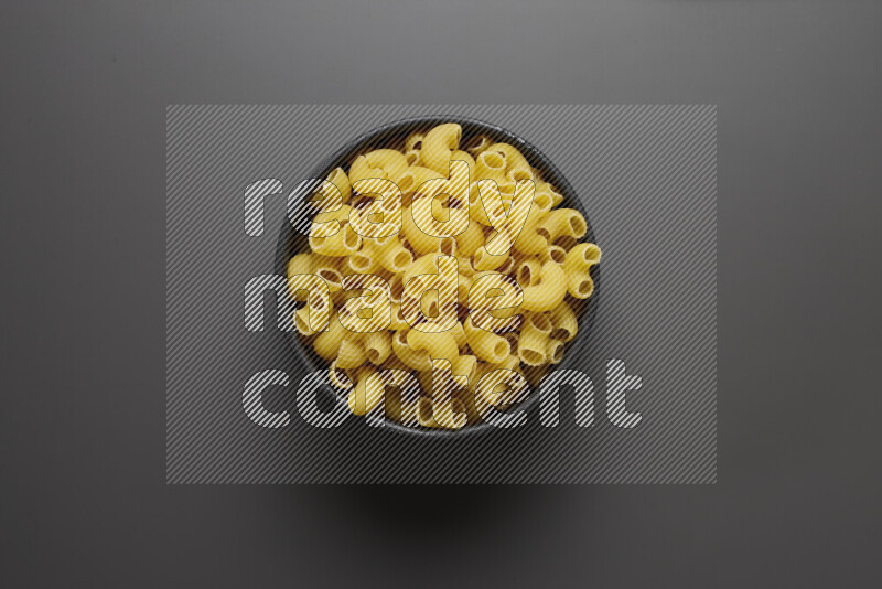 Elbow pasta in a pottery bowl on grey background