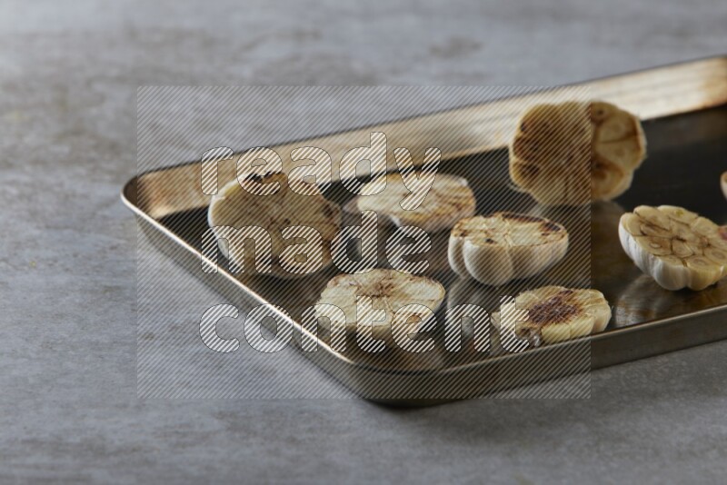half's roasted garlic in a stainless tray on a grey textured countertop