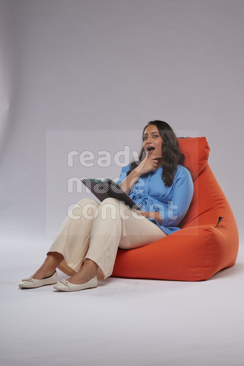 A woman sitting on an orange beanbag and reading a book
