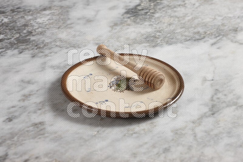 Decorative pottery plate with wooden honey dipper in it on grey marble background