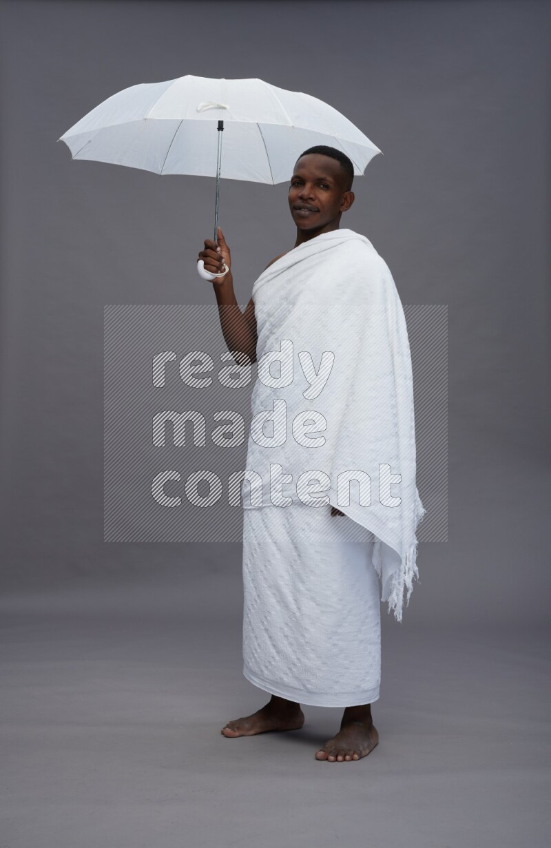 A man wearing Ehram Standing holding umbrella on gray background