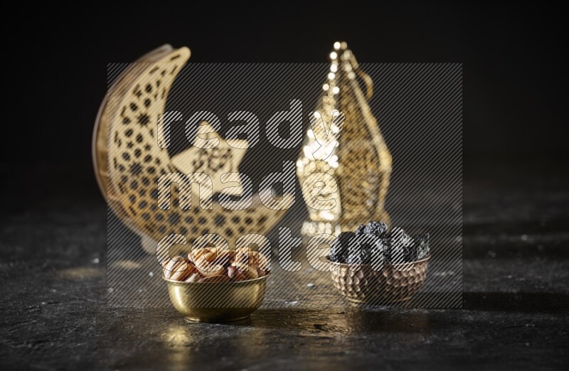 Nuts in a metal bowl with dried plums beside golden lanterns in a dark setup