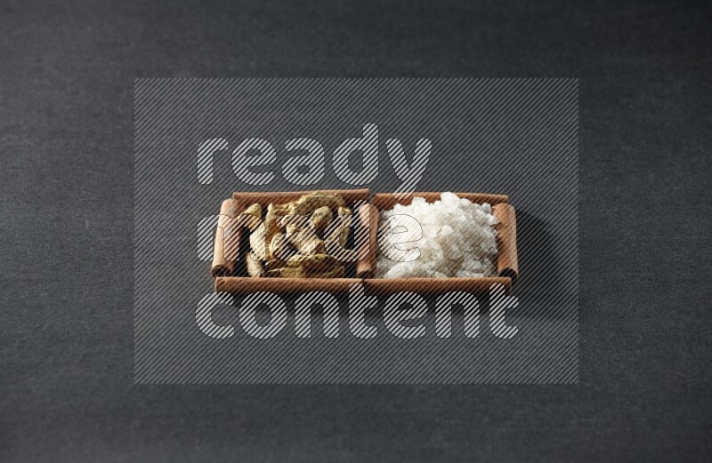 2 squares of cinnamon sticks full of white salt and turmeric fingers on black flooring